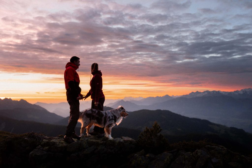 Sonnenaufgang in der Zentralschweiz. Ein Paar und ein Australian Shepherd Hund stehen augf einem felsen. 