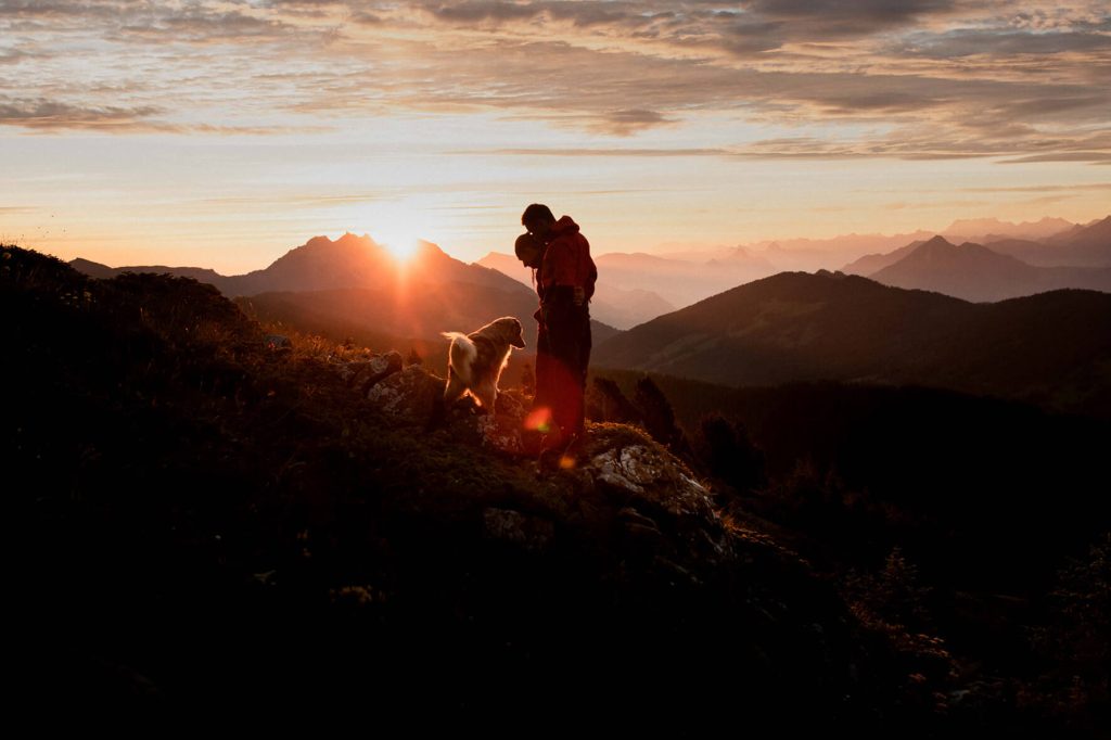 Sonnenaufgang hinter dem Pilatus. Ein Paar mit Hund stehen auf einem Felsen in den Schweizer Alpen. 